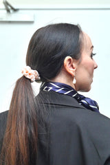 Kvinde iført LA SUIT produkter, herunder lyserød silke scrunchie, marineblå silketørklæde og sort habitjakke set fra bagfra.