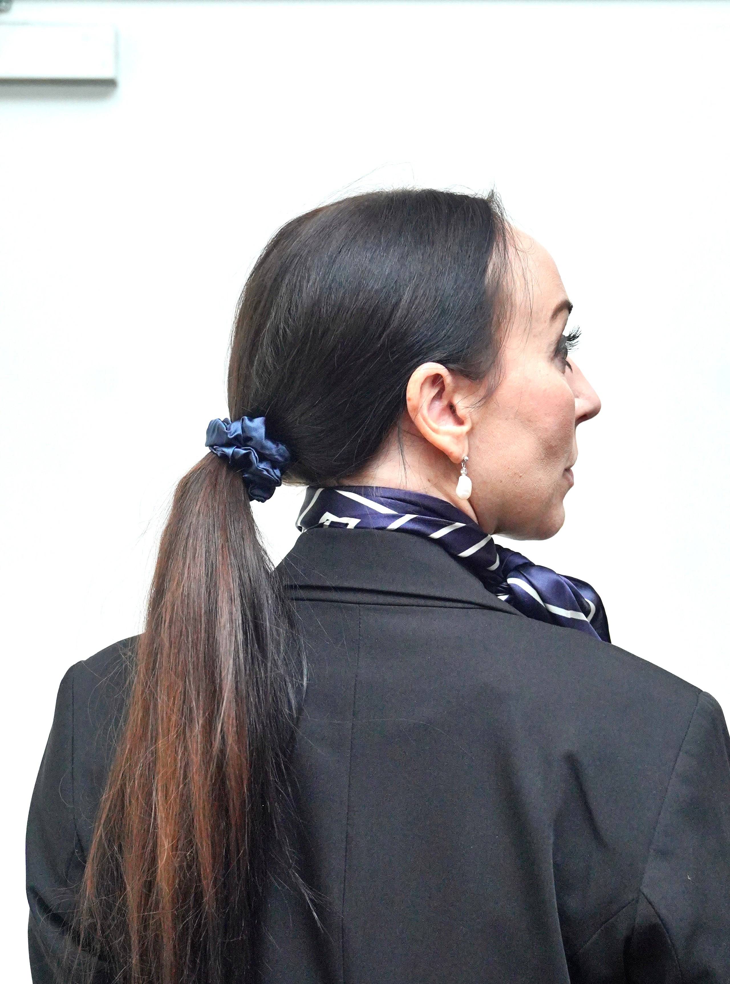 Kvinde iført LA SUIT produkter, herunder marineblå silke scrunchie, marineblå silketørklæde og sort habitjakke set fra siden.