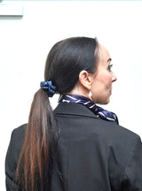 Kvinde iført LA SUIT produkter, herunder marineblå silke scrunchie, marineblå silketørklæde og sort habitjakke set fra siden.